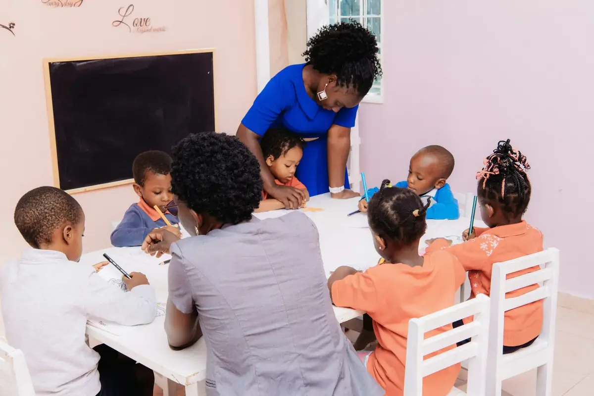 A teacher leaning over a table of young pupils as they draw.