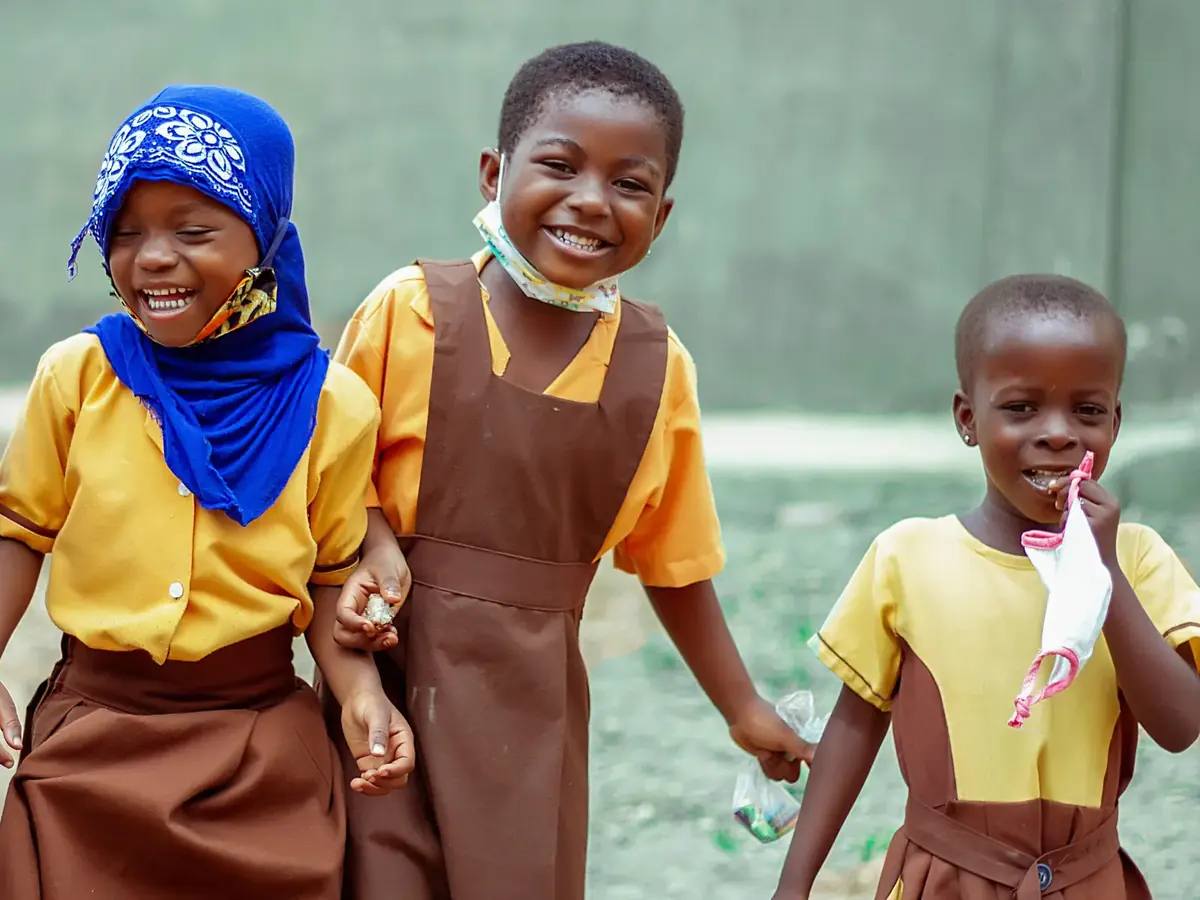 Three primary school pupils in uniform, laughing on their way across the playground.