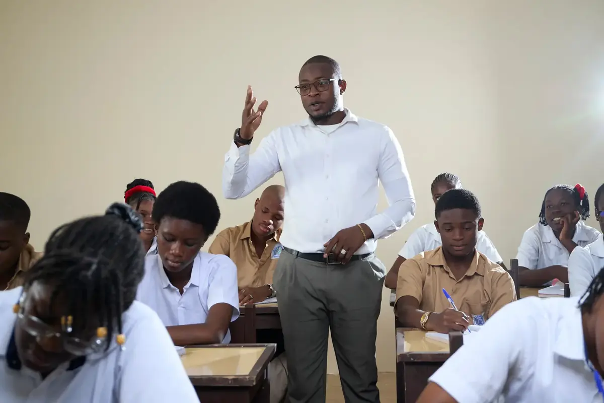 A teacher mid-lesson, standing among secondary pupils at their desks.